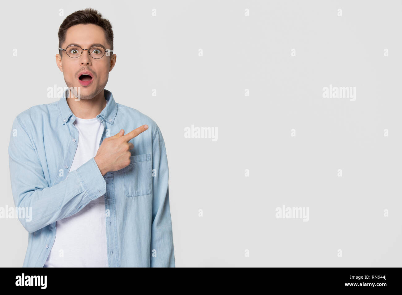 Shocked stunned young man nerd pointing finger aside at copyspace Stock Photo