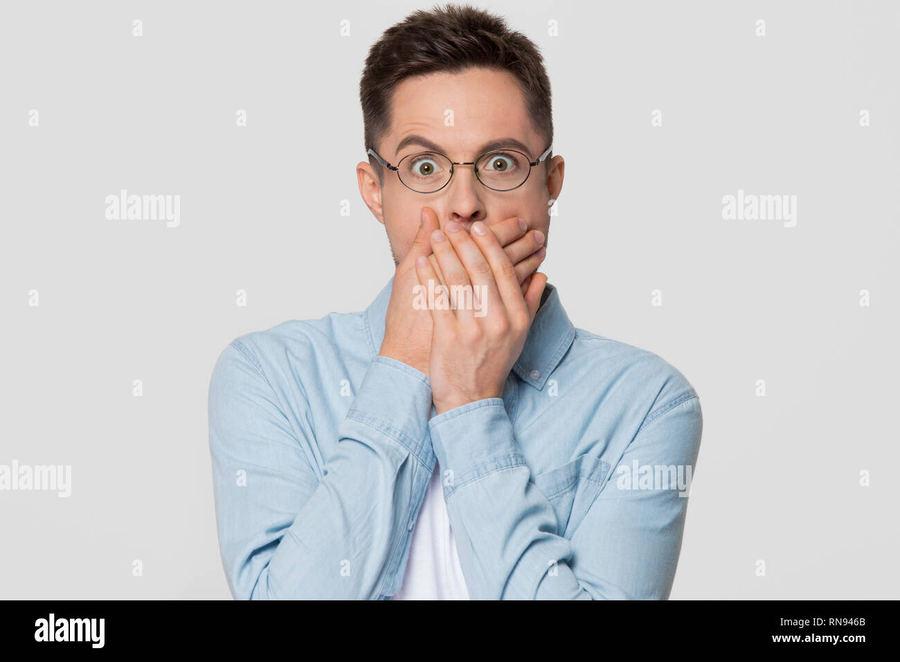 Shocked scared man with surprised face covering mouth with hands Stock Photo
