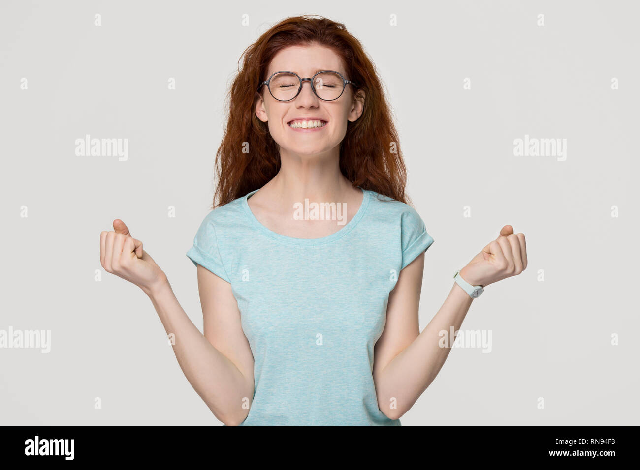Happy overjoyed red-haired woman in glasses celebrating win success Stock Photo