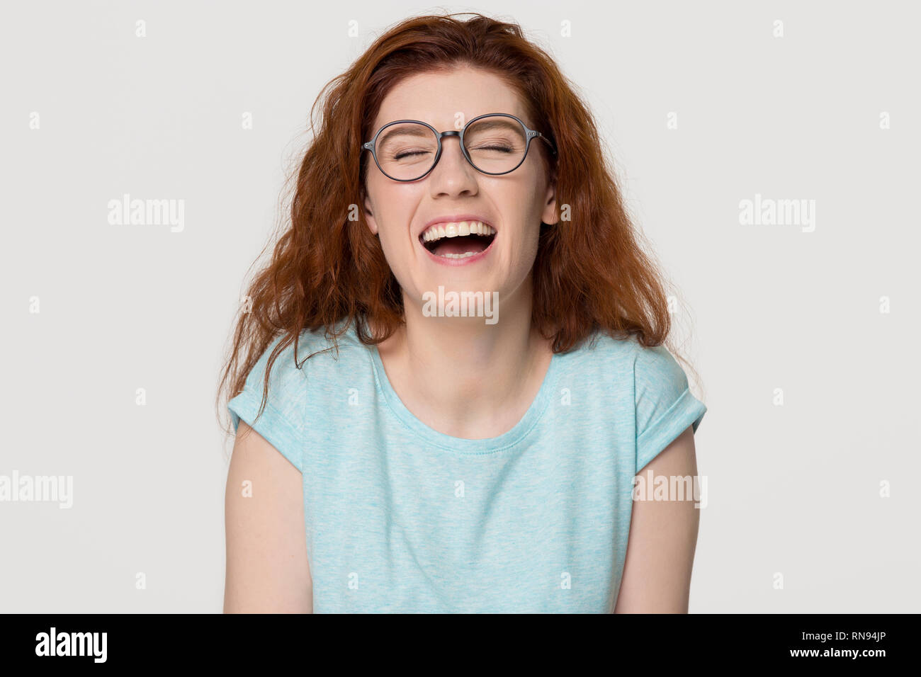 Cheerful happy red-haired young woman in glasses laughing out loud Stock Photo
