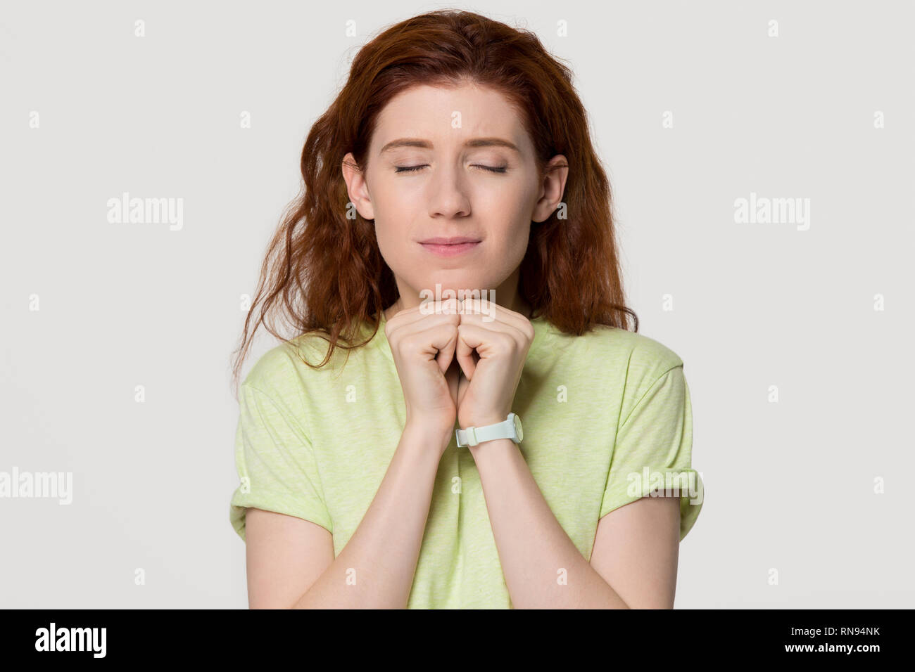 Hopeful redhead woman clenching fists making wish isolated on background Stock Photo