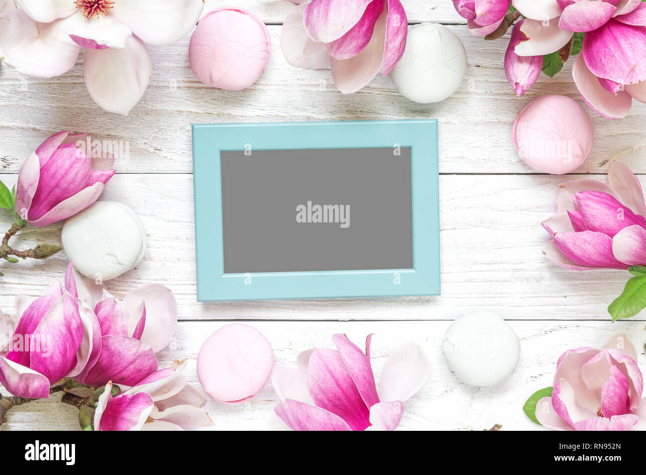 blank photo card in frame made of pink magnolia flowers and marshmallows on white wooden background. flat lay. top view. mock up. wedding or womens da Stock Photo