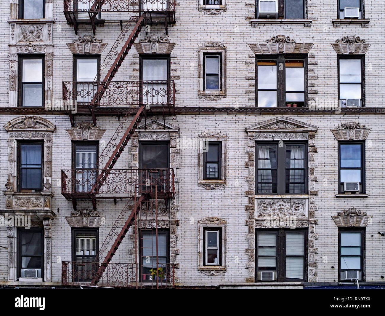 old New York apartment building with external fire escapes, window air conditioners, and ornate trim around windows Stock Photo
