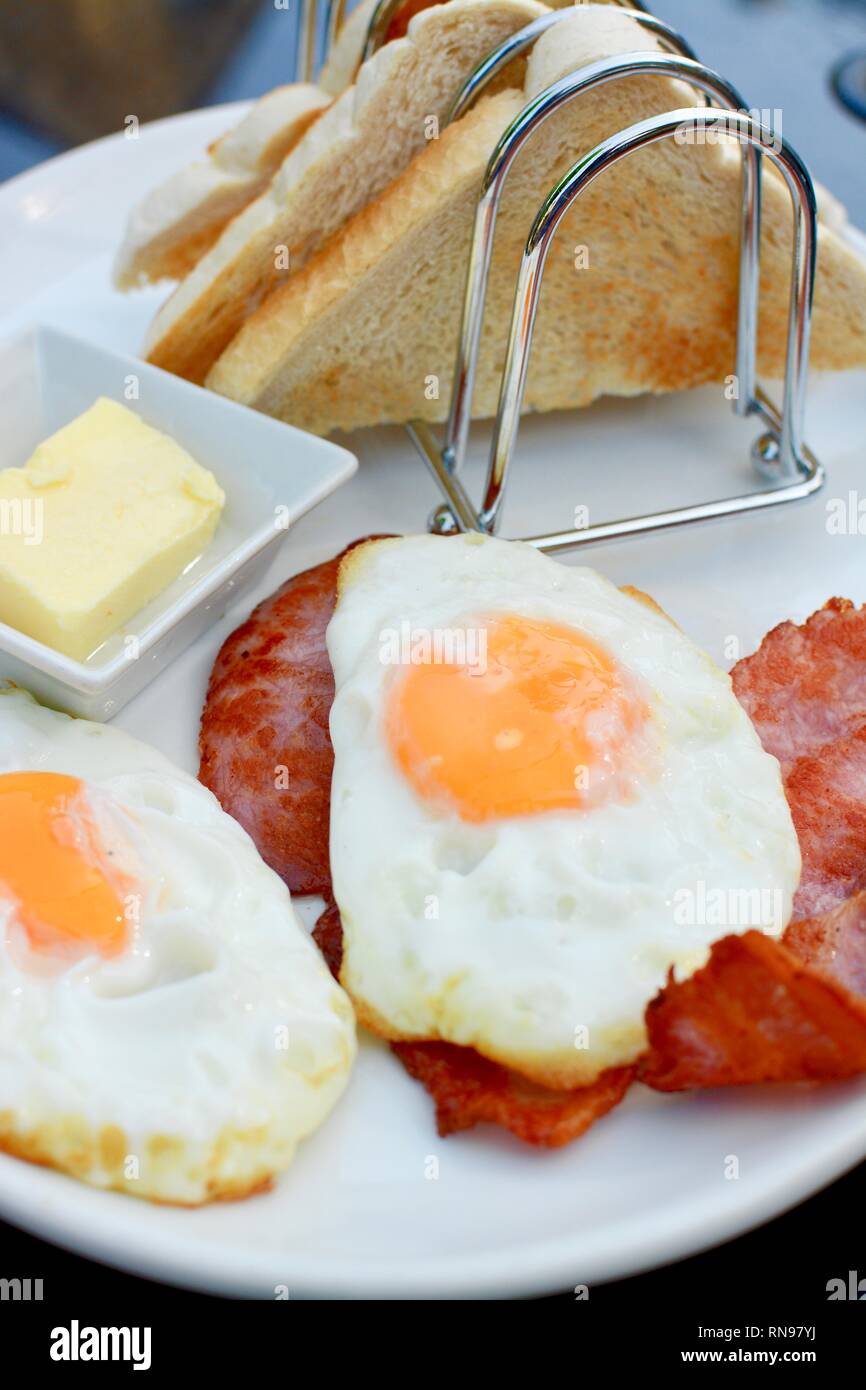 Breakfast with fried eggs, bacon, toast and rack, butter all served on a white plate Stock Photo