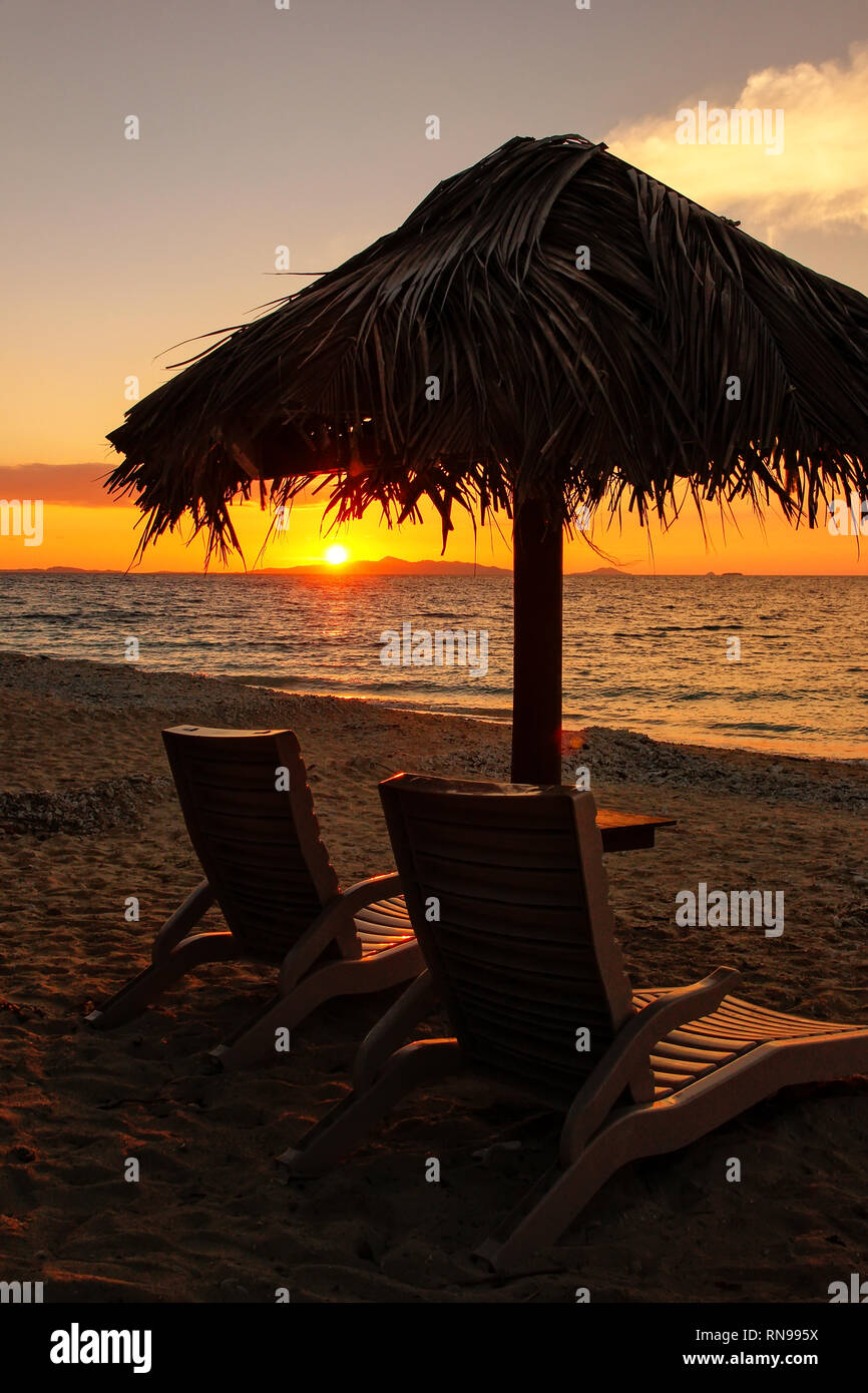 Silhouetted sun chairs with thatched umbrella on a beach at sunrise, South Sea Island, Mamanuca group, Fiji. Stock Photo