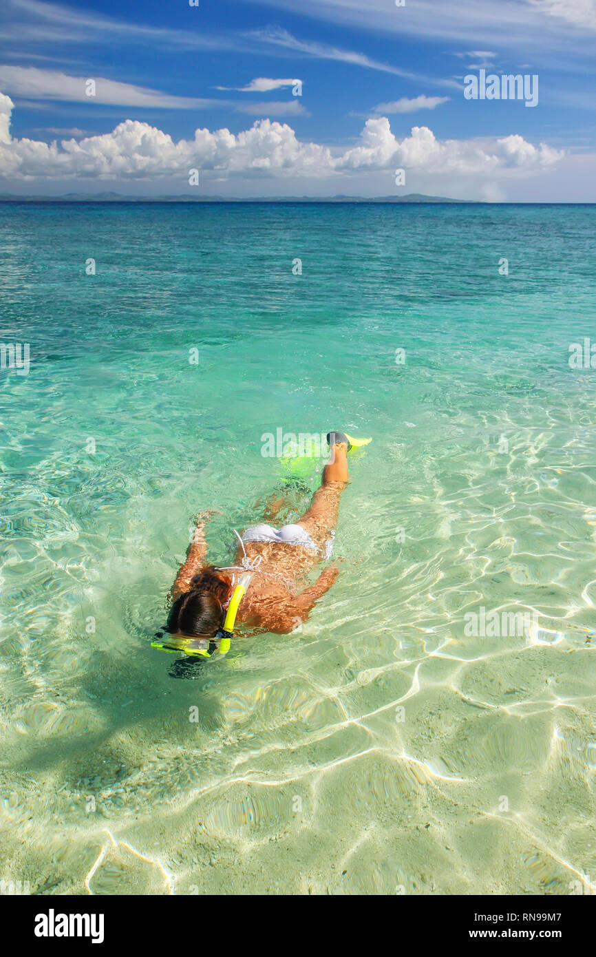 Young woman snorkeling in clear shallow water near tropical island