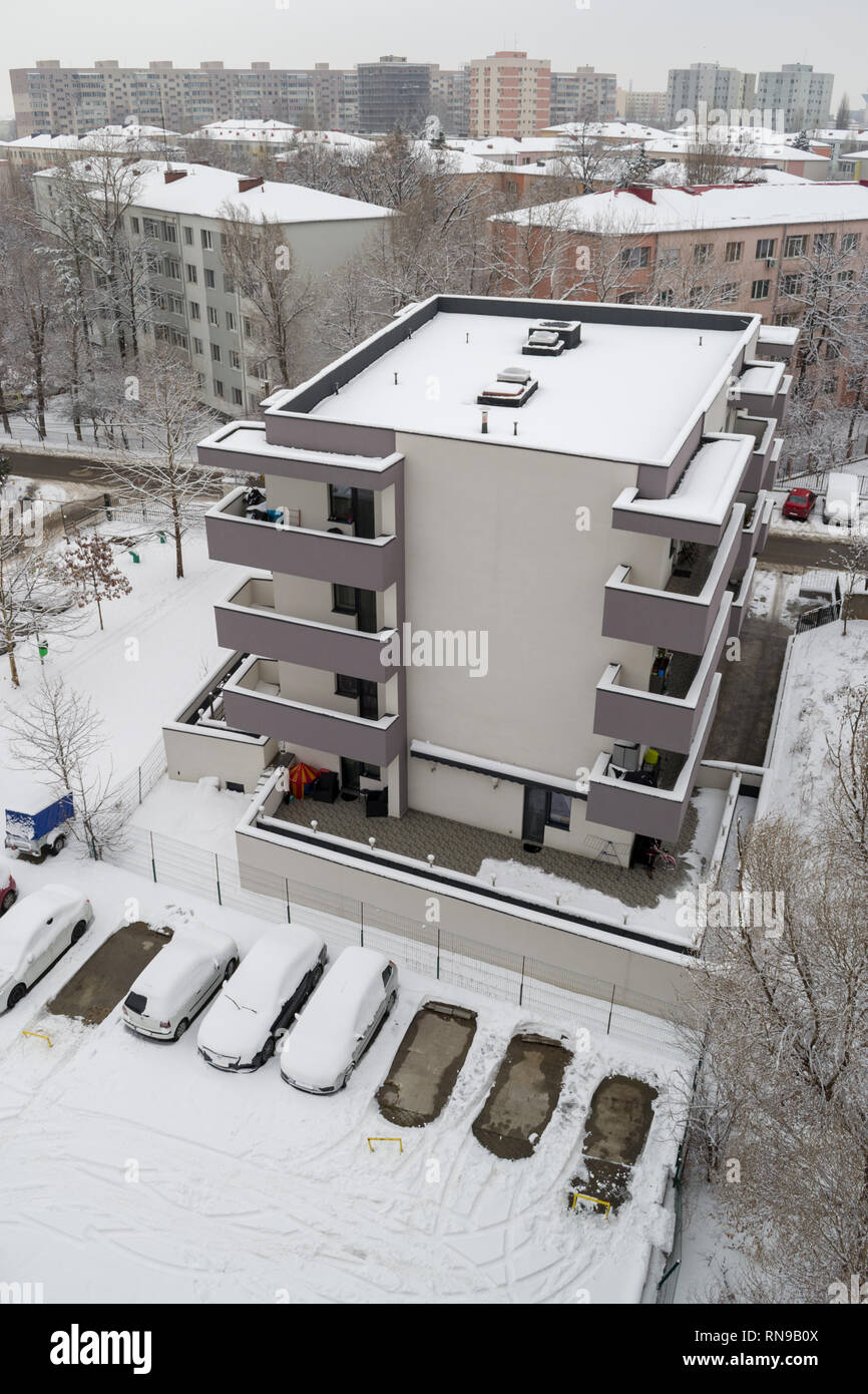 Top view of an apartment building in Winter, after a heavy snow, with parked cars covered in snow and empty parking spots next to it. Bucharest, Roman Stock Photo