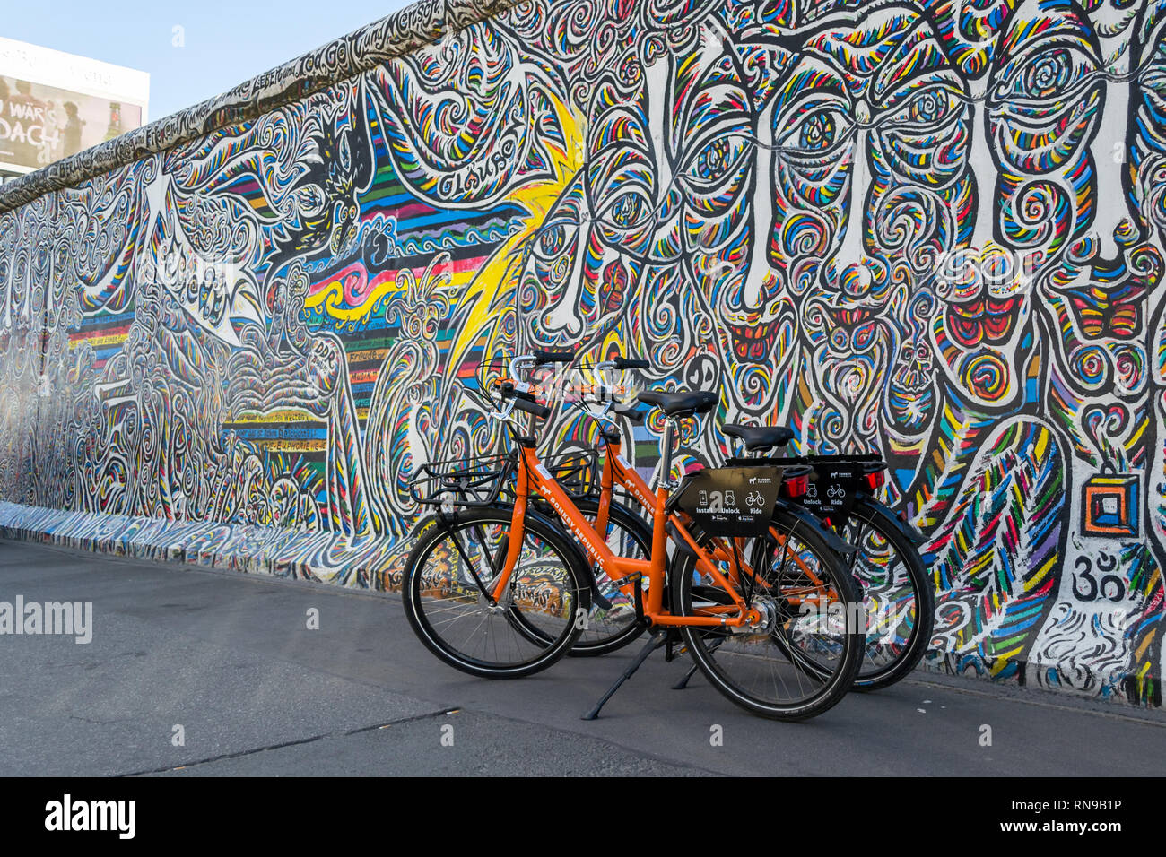 Berlin / Germany - 30 June 2018: Orange dock-less bikes for hire at East Side Gallery, a 1316 m long remnant of the Berlin Wall painted with graffiti  Stock Photo
