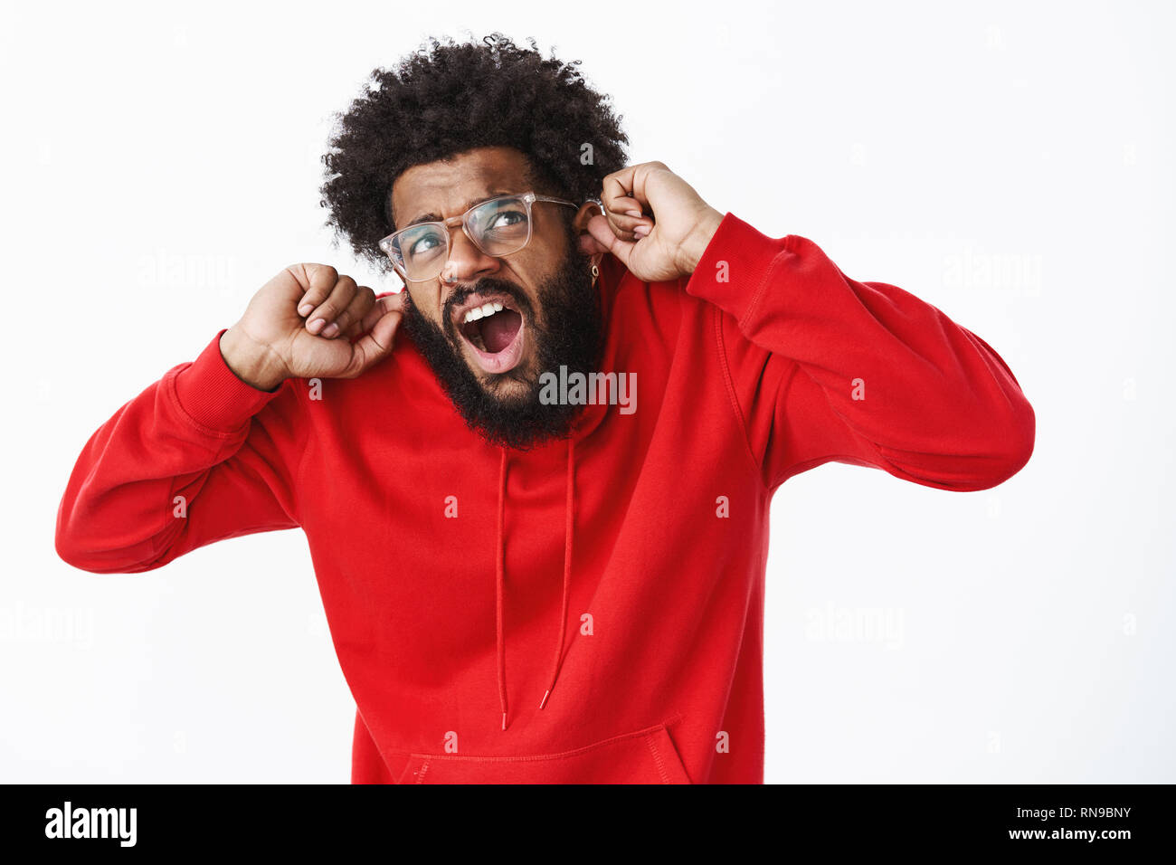 Studio shot of disturbed guy suffering from discomfort as compaining on loud neighbours being irritated by noise and annoying music yelling closing Stock Photo