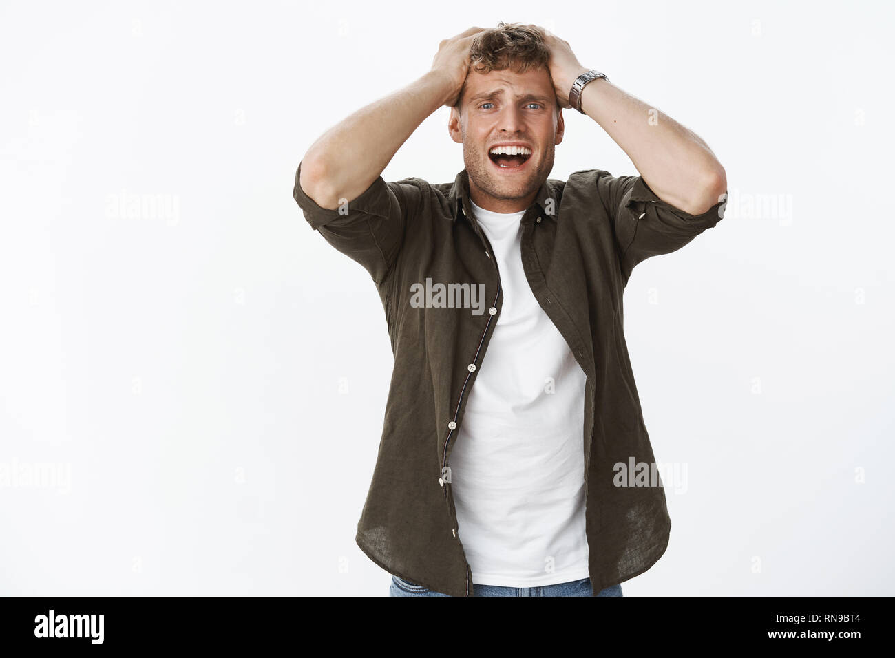 Guy losing everything standing in despair and panic pulling hair of head yelling suffering painful heartbreak, grimacing in sorrow and disappointed Stock Photo