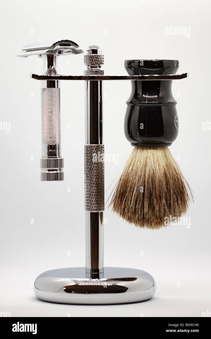 Stainless steel double edge safety razor and badger hair shaving brush hanging from polished stainless steel stand on gray background Stock Photo