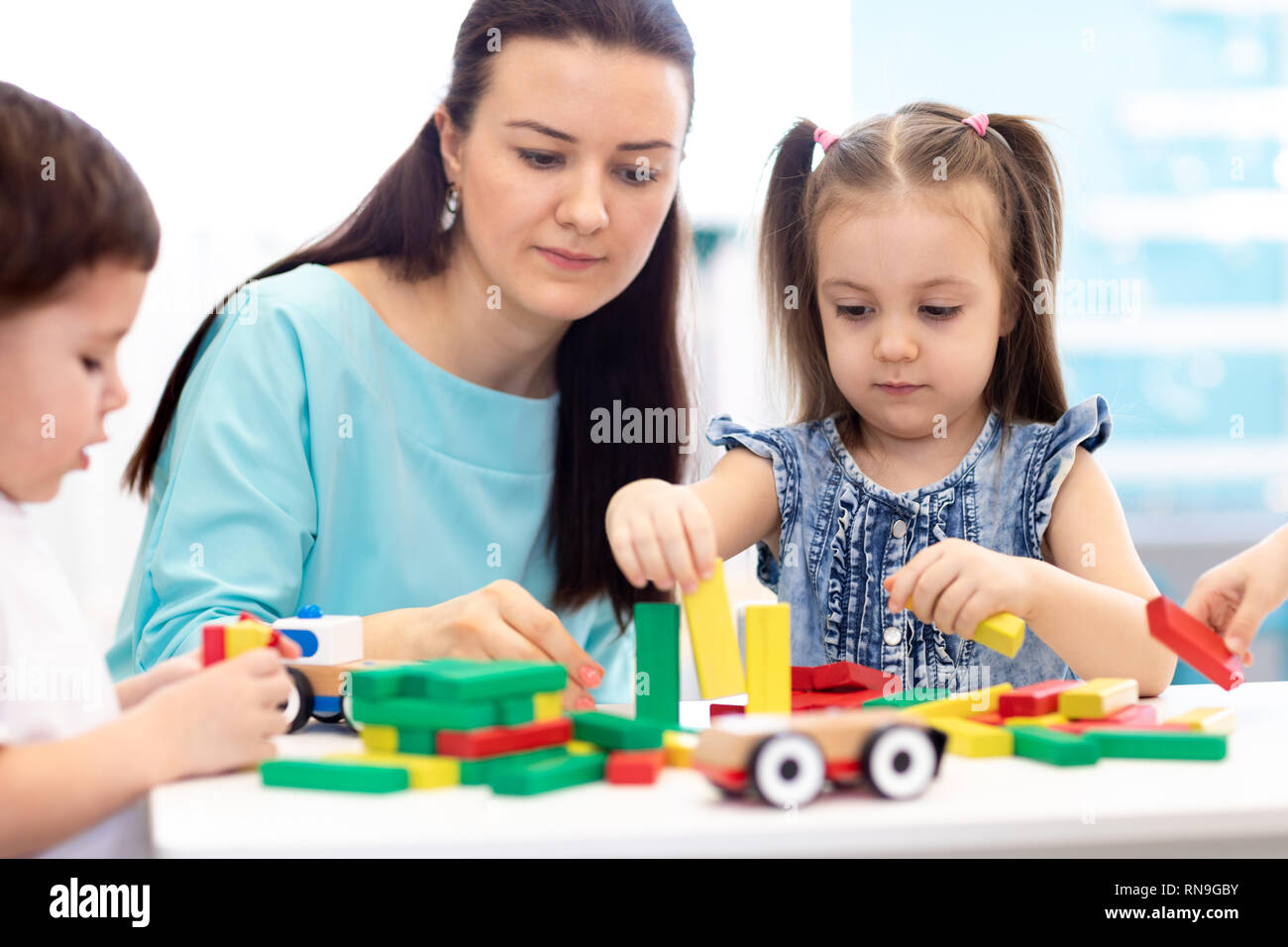 Little children building block toys with carer at home or daycare. Kids playing with color