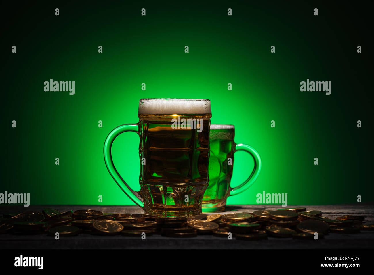 glasses of irish beer standing near golden coins on green background