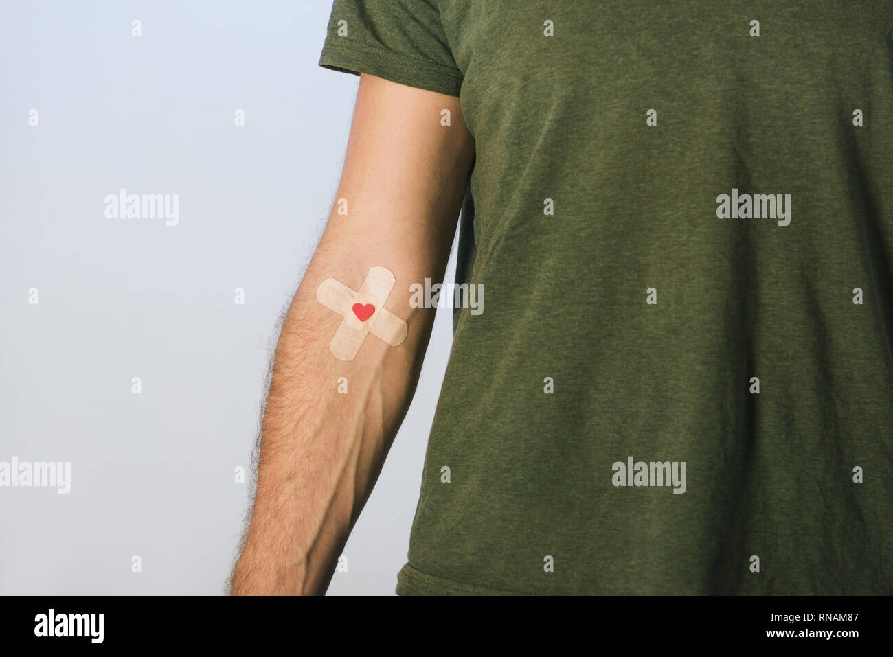 Partial view of patient in green t-shirt with plasters on grey background, blood donation concept Stock Photo