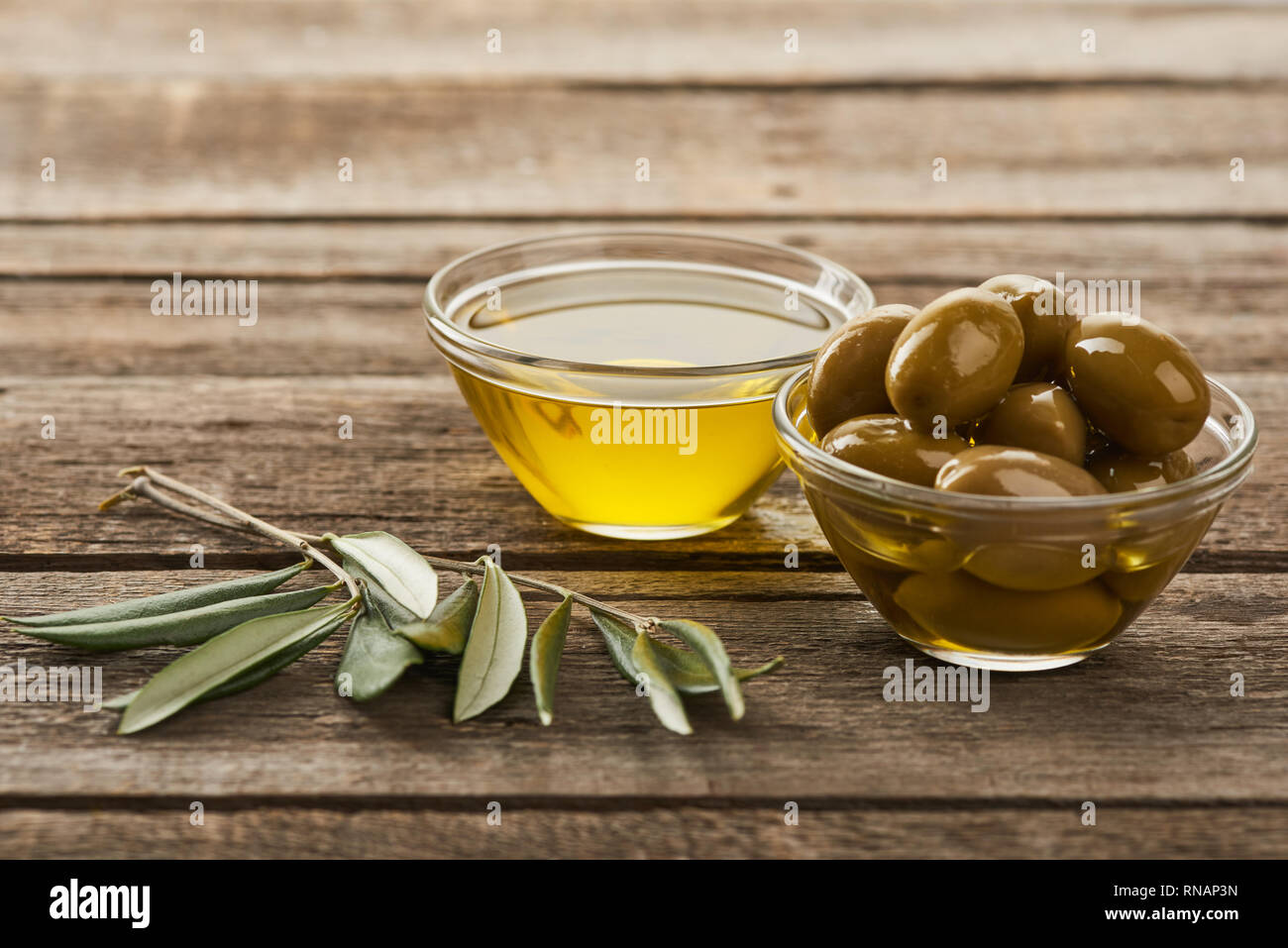 glass bowls with olives and oil, and olive tree branch on wooden ...