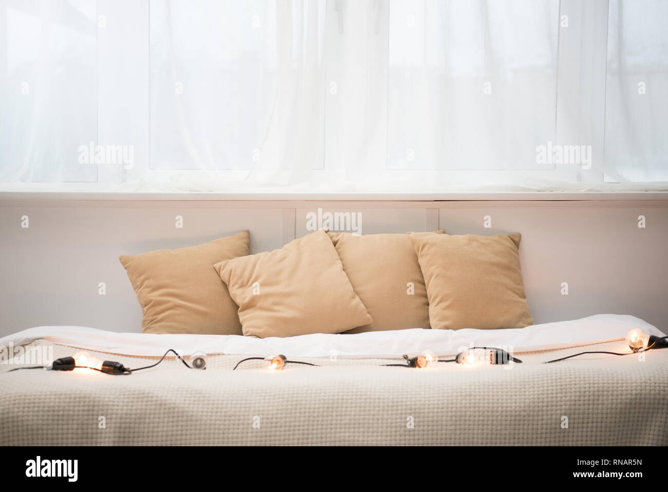 empty bed with brown pillows, white blanket and festoon lights Stock Photo