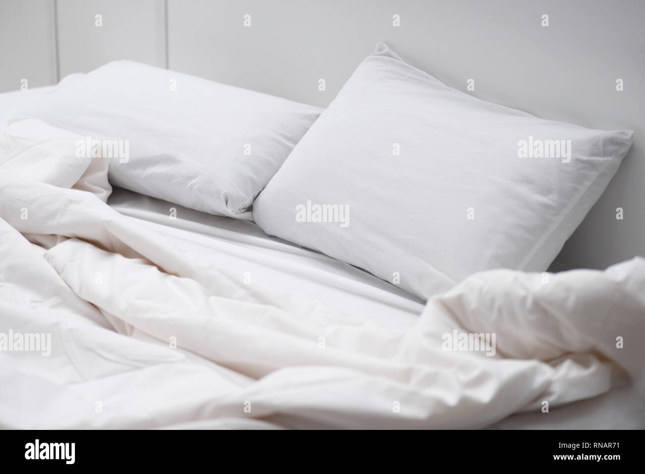 empty-bed-with-white-pillows-and-blanket-RNAR71