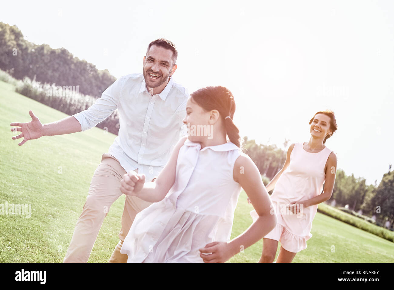 Bonding. Family of three running on grassy field playing playing touch and run game smiling playful Stock Photo