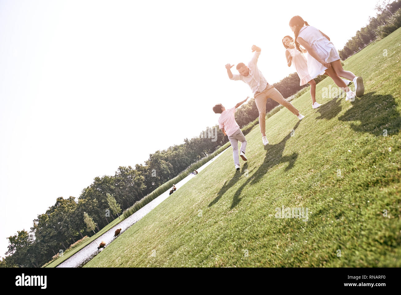 Bonding. Family of four running on grassy field playing playing touch and run game laughing cheerful Stock Photo