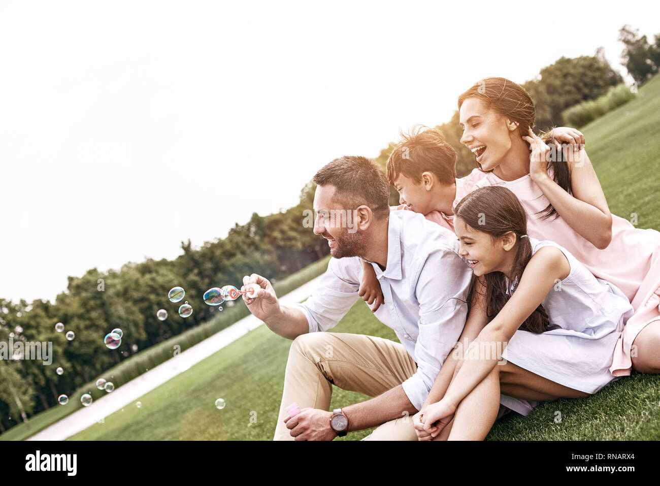 Bonding. Family of four sitting on a grassy field blowing bubbles smiling happy Stock Photo