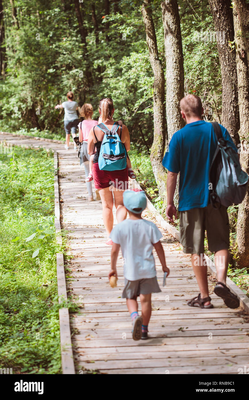 Family going a path in forest. Mother, father, boy and girl spending time together, vacations close to nature Stock Photo
