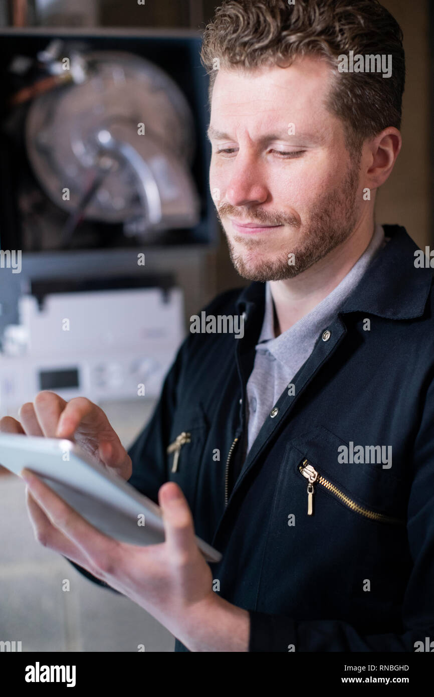 Male Heating Engineer Servicing Central Heating Boiler Using Digital Tablet Stock Photo