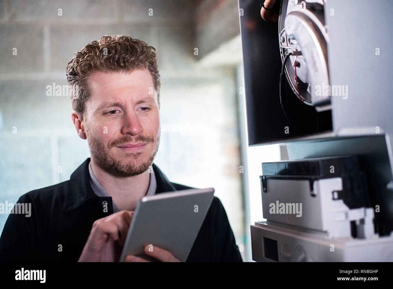 Male Heating Engineer Working On Central Heating Boiler Using Digital Tablet Stock Photo