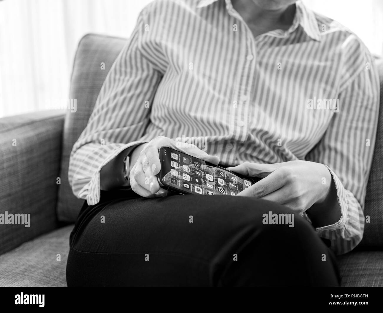 PARIS, FRANCE - SEP 27, 2018: Elegant French woman testing the newest latest iPhone Xs and Xs Max smartphone telephone from Apple Computers on office living room sofa - black and white Stock Photo