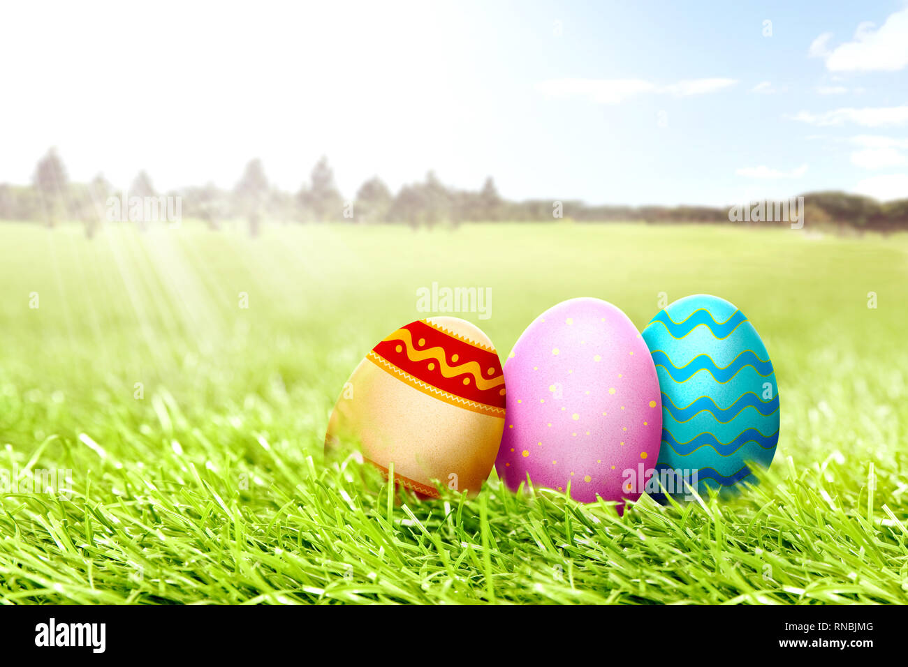 Colorful easter eggs on the grass field with trees and blue sky background. Happy Easter Stock Photo