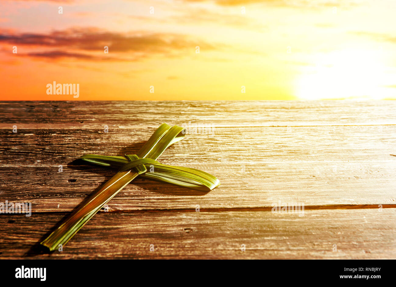 Cross shape of palm leaf on wooden table with rays of sunset background. Palm Sunday concept Stock Photo