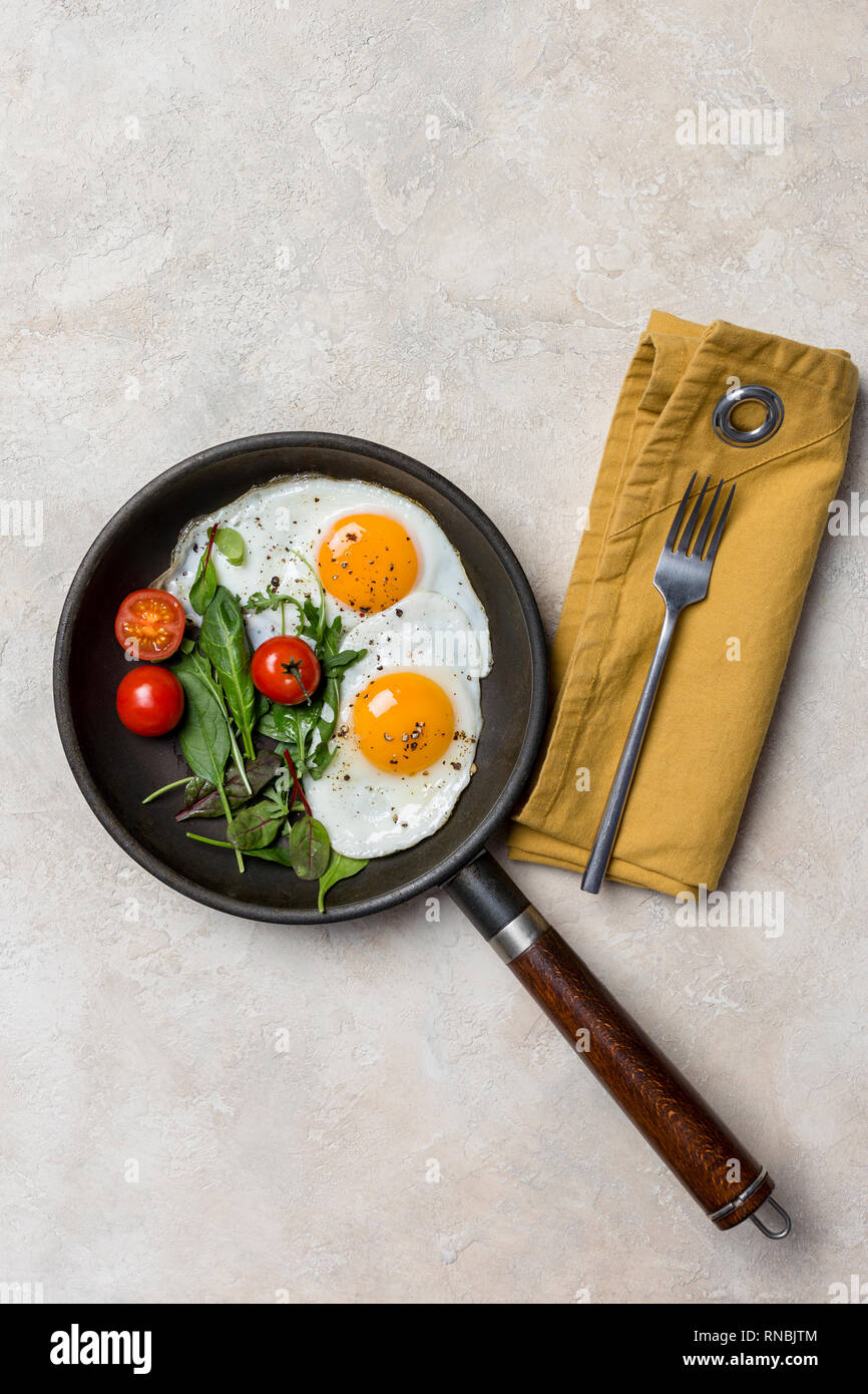 Pan and fried eggs for breakfast with herbs at beige background