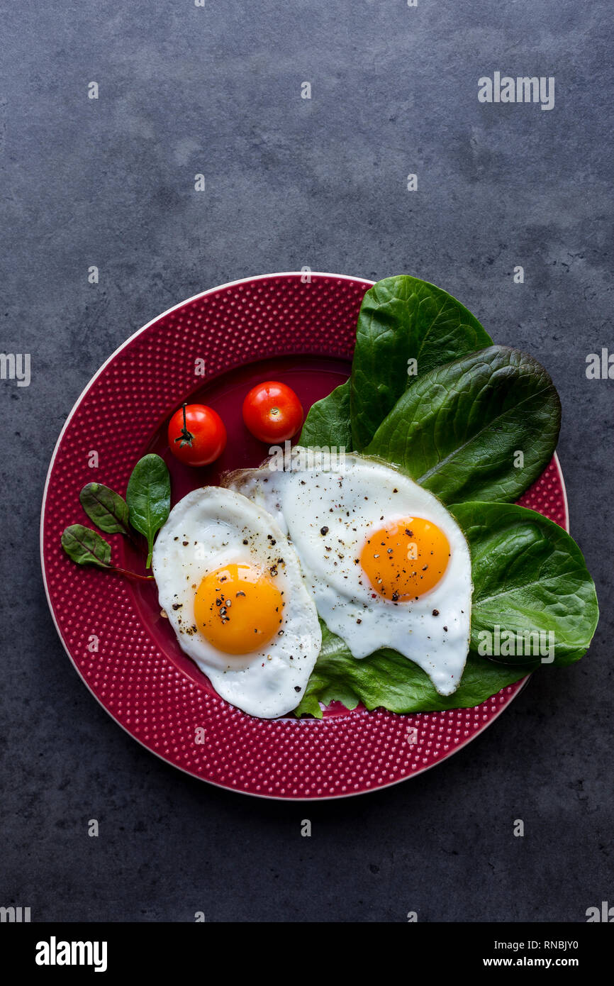 Two fried eggs with salad on red plate on dark grey background. Horizontal view form above Stock Photo