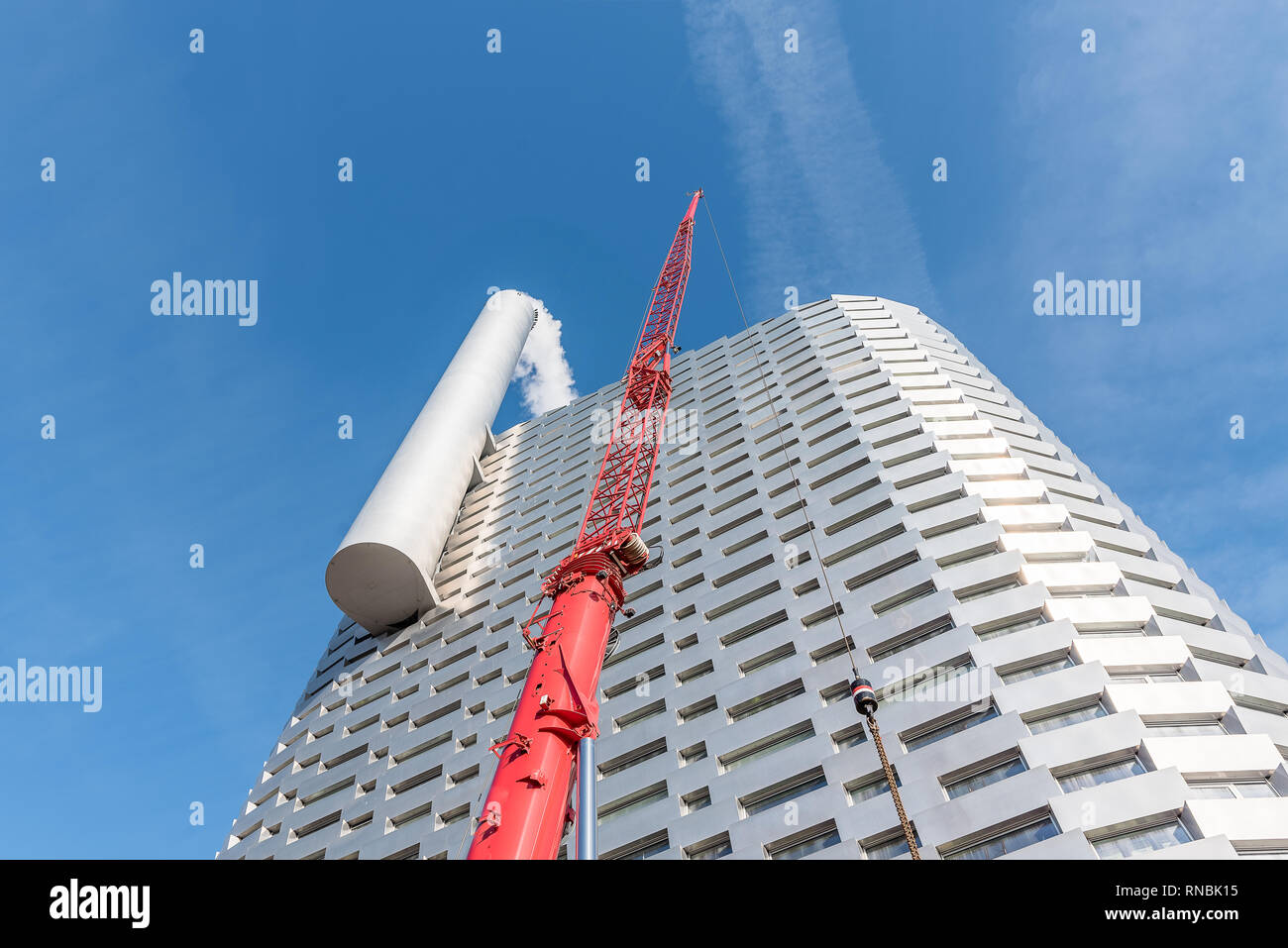 A red crane over the Amager Ressource Center, a futuristic incinerator with a big chimney, that can blow smoke rings, Copenhagen, February 16, 2019 Stock Photo