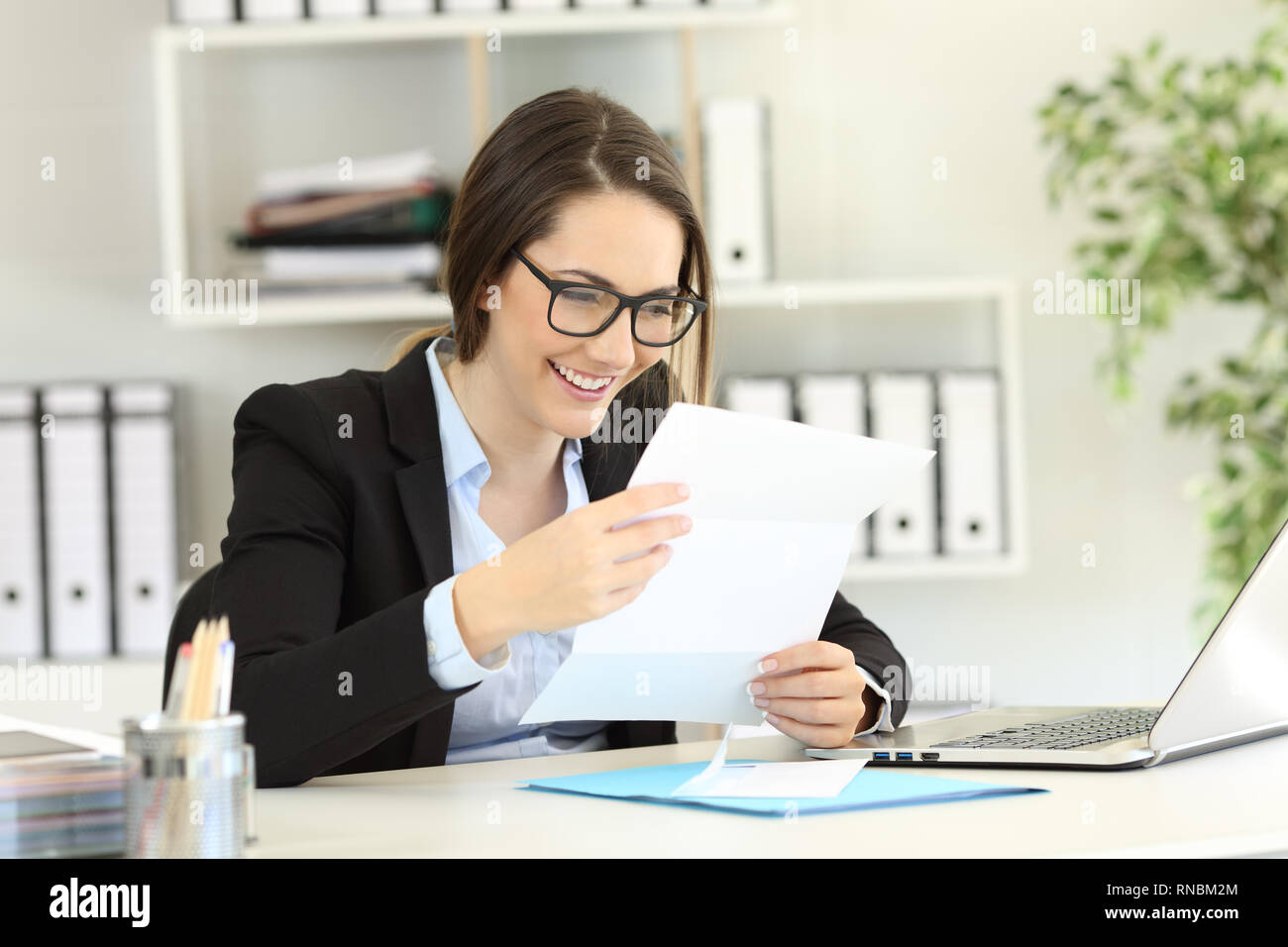 Happy office worker reading a paper letter in a desktop Stock Photo