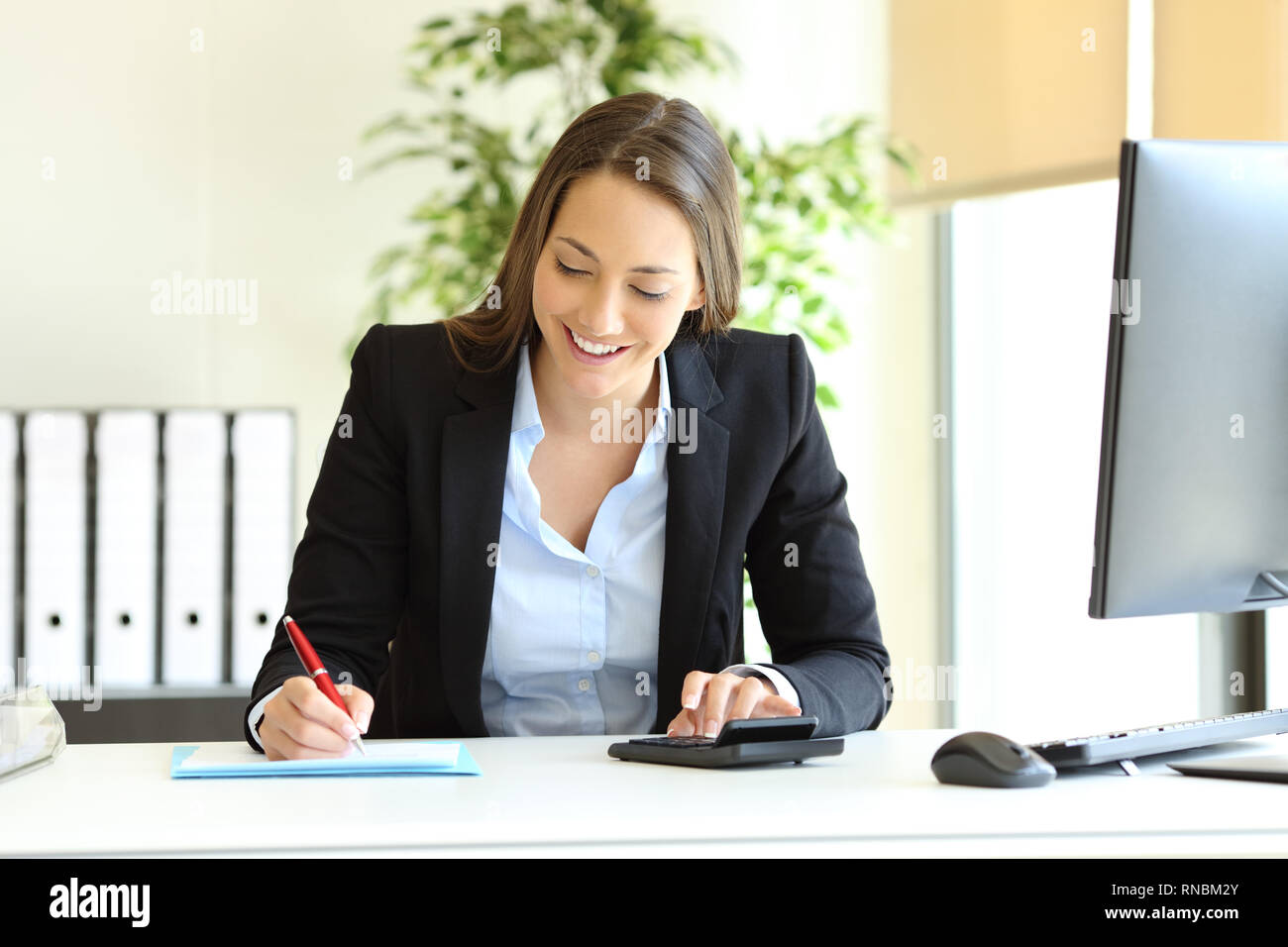 Office worker calculating budget using calculator and writing on a document Stock Photo