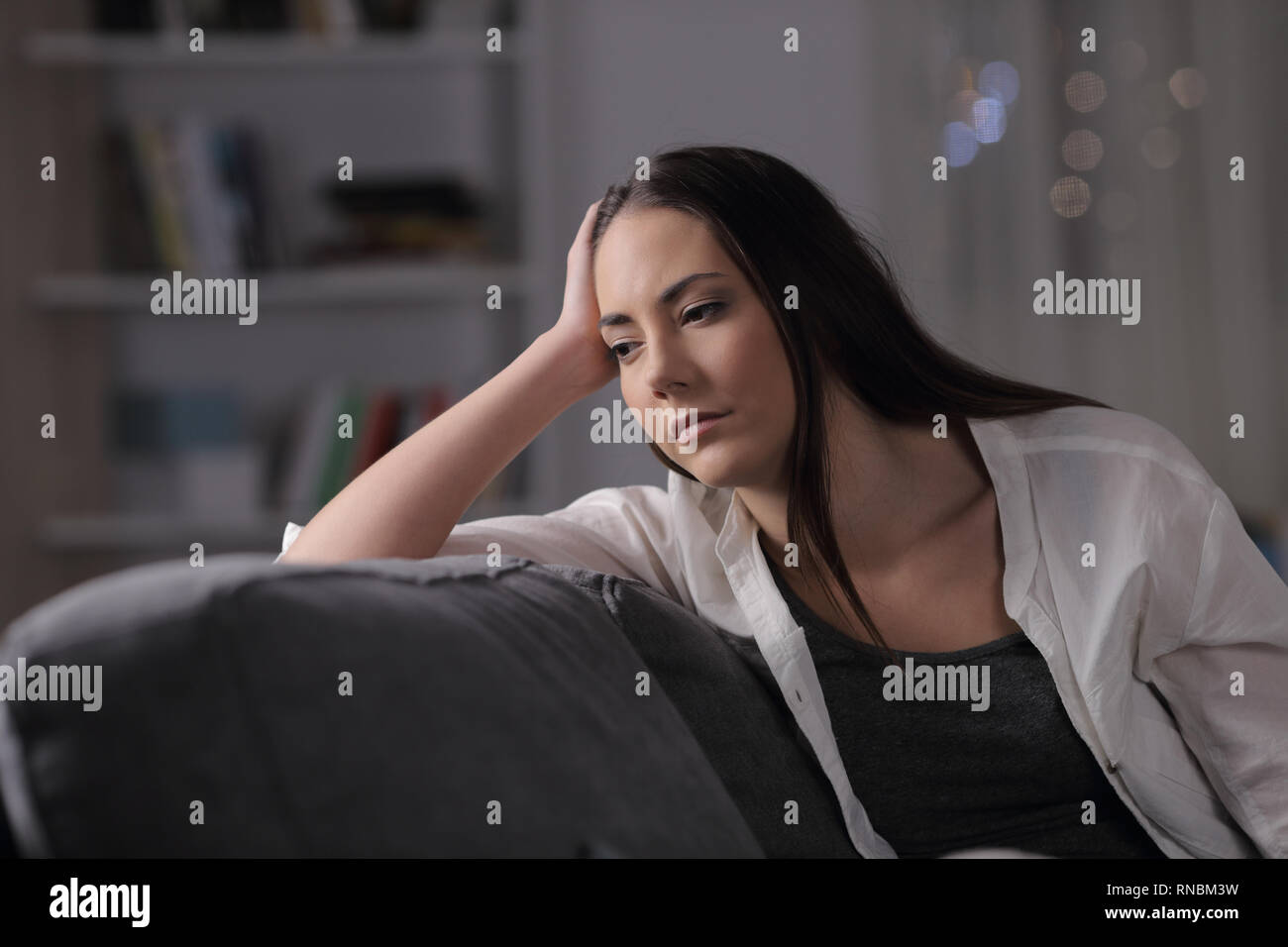 Sad woman looks away sitting on a couch in the night at home Stock ...