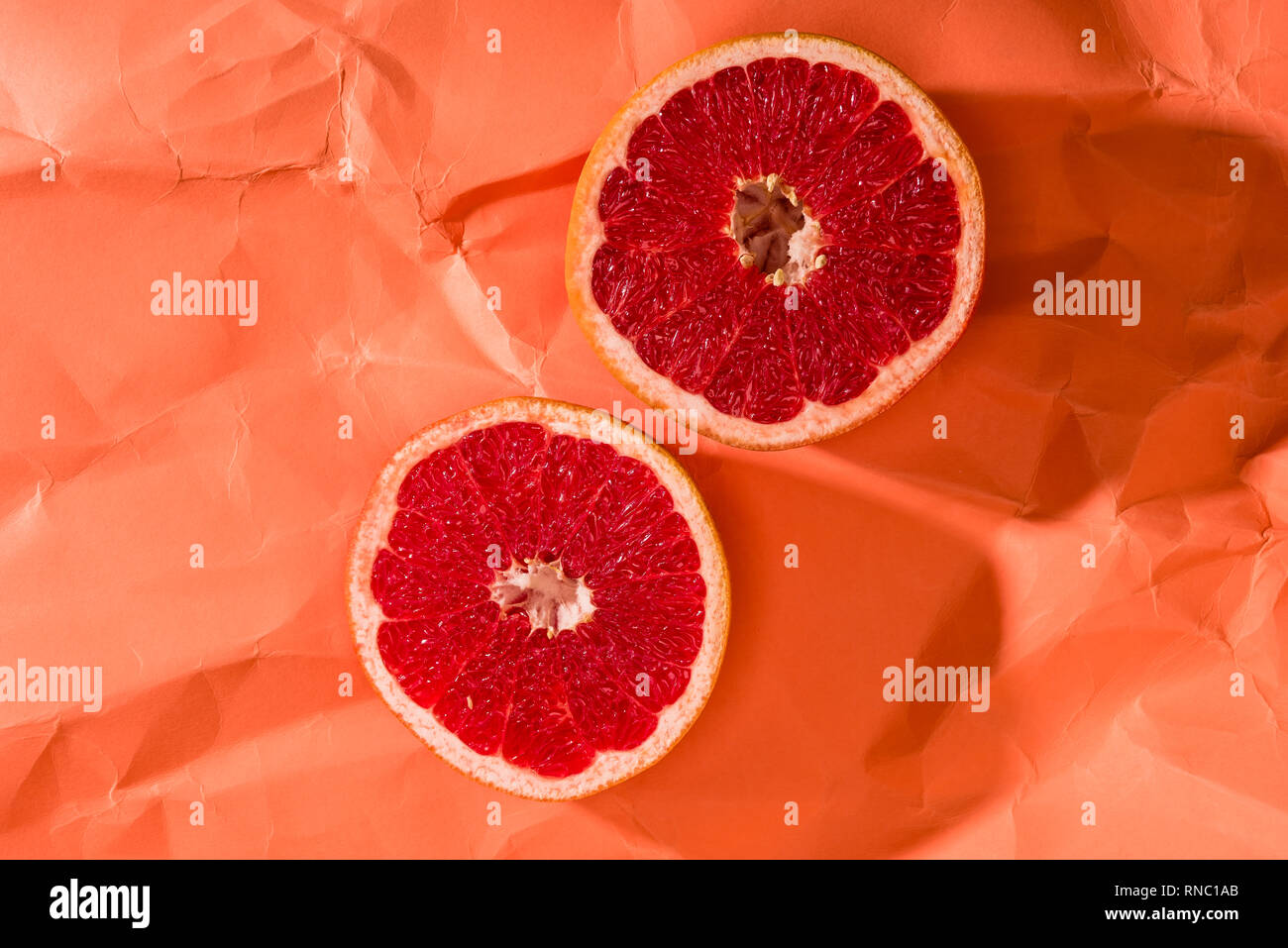grapefruit halves on crumpled paper textured coral surface, color of ...