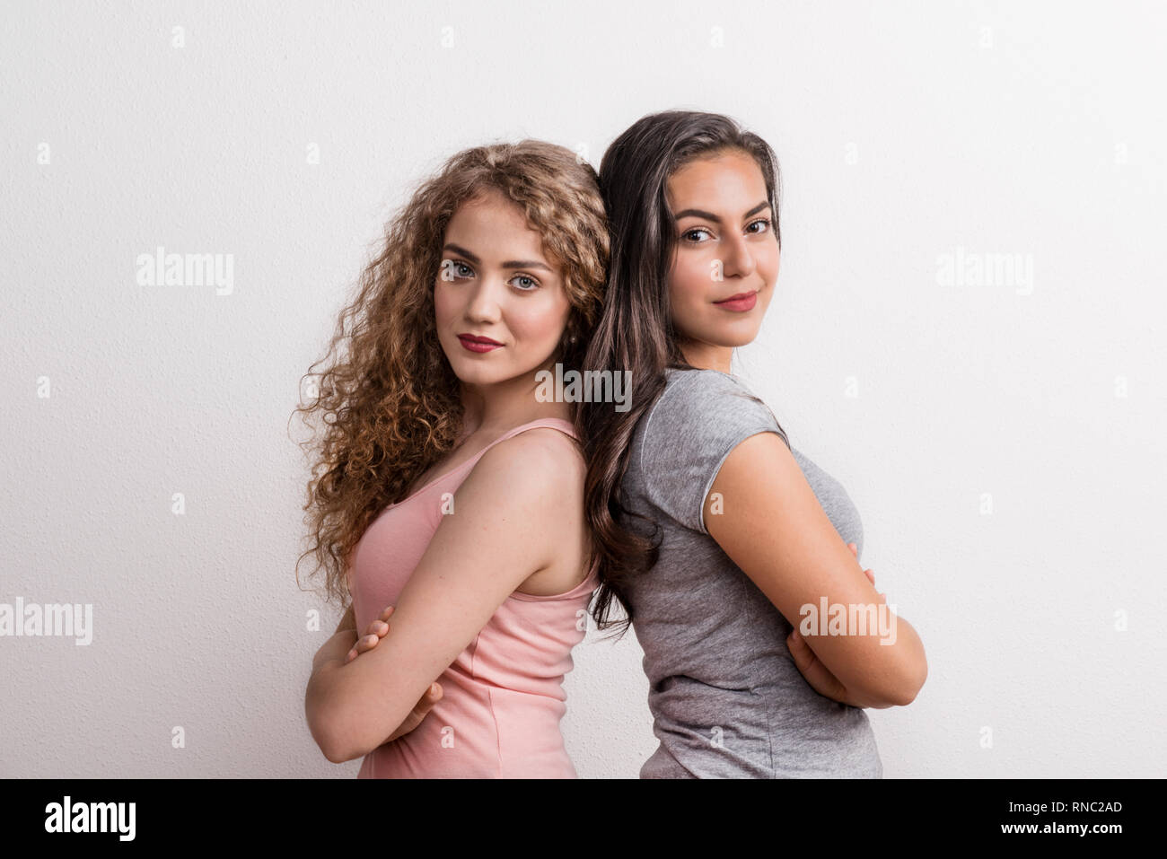 Young beautiful women in studio, standing back to back with arms crossed. Stock Photo