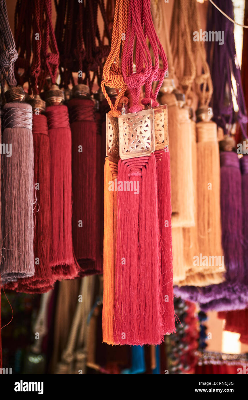 Colourful tassels pinned by metal medallions hanging in a market stall in Marrakech. Stock Photo