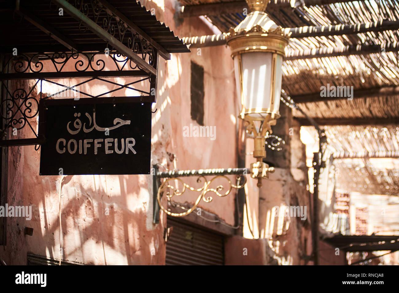 The shop front of a hairdresser ( coiffeur ) in a passage way in the medina souq of Marrakech.  The signage is in French and Islamic or Arabic. Stock Photo