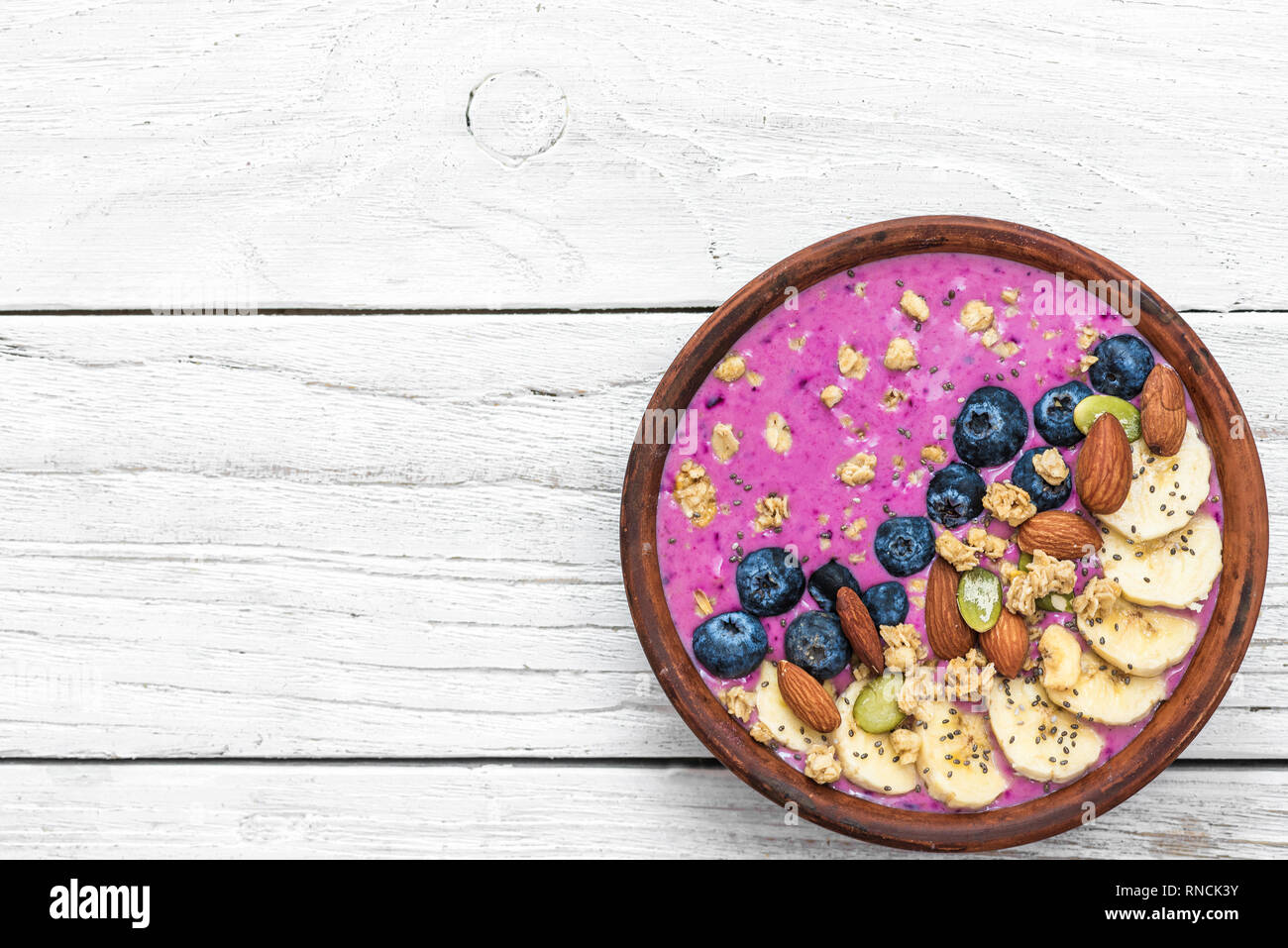 Healthy vegan breakfast. acai smoothie bowl with blueberry, fruits, granola, almonds, pumpkin and chia seeds on white wooden table. detox food concept Stock Photo