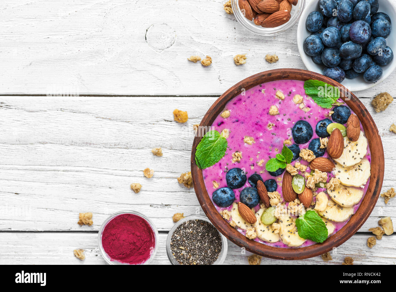 Smoothie bowl with fresh berries, nuts, seeds, granola and mint for healthy vegan diet breakfast on white wooden table. top view with copy space Stock Photo