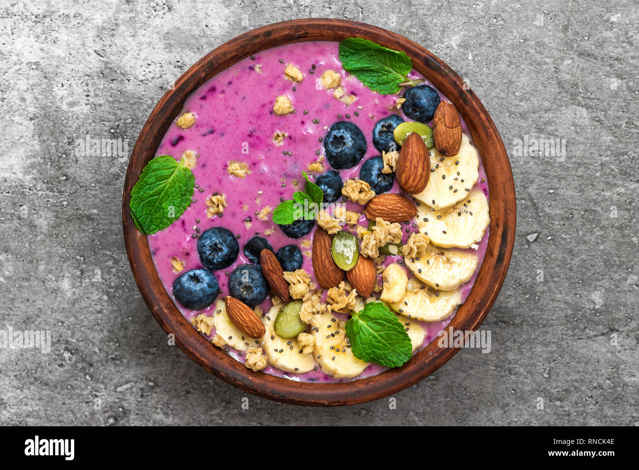 Acai smoothie bowl topped with banana, chia and pumpkin seed, blueberry, almonds and granola. healthy vegan breakfast. top view Stock Photo