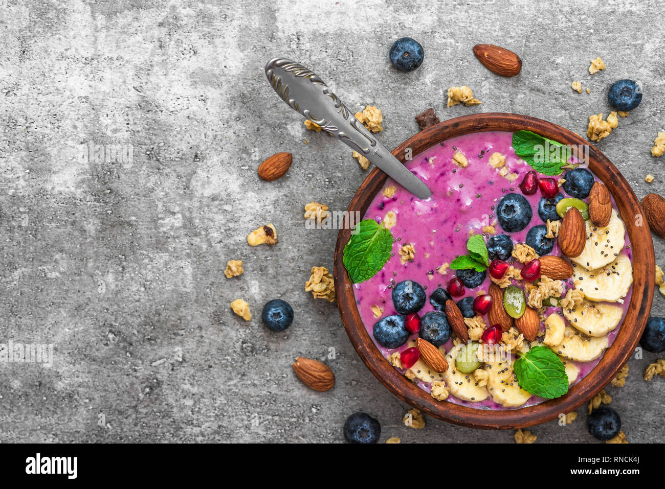 Acai smoothie bowl topped with banana, chia and pumpkin seed, blueberry, almonds and granola with spoon. healthy vegan breakfast. top view with copy s Stock Photo