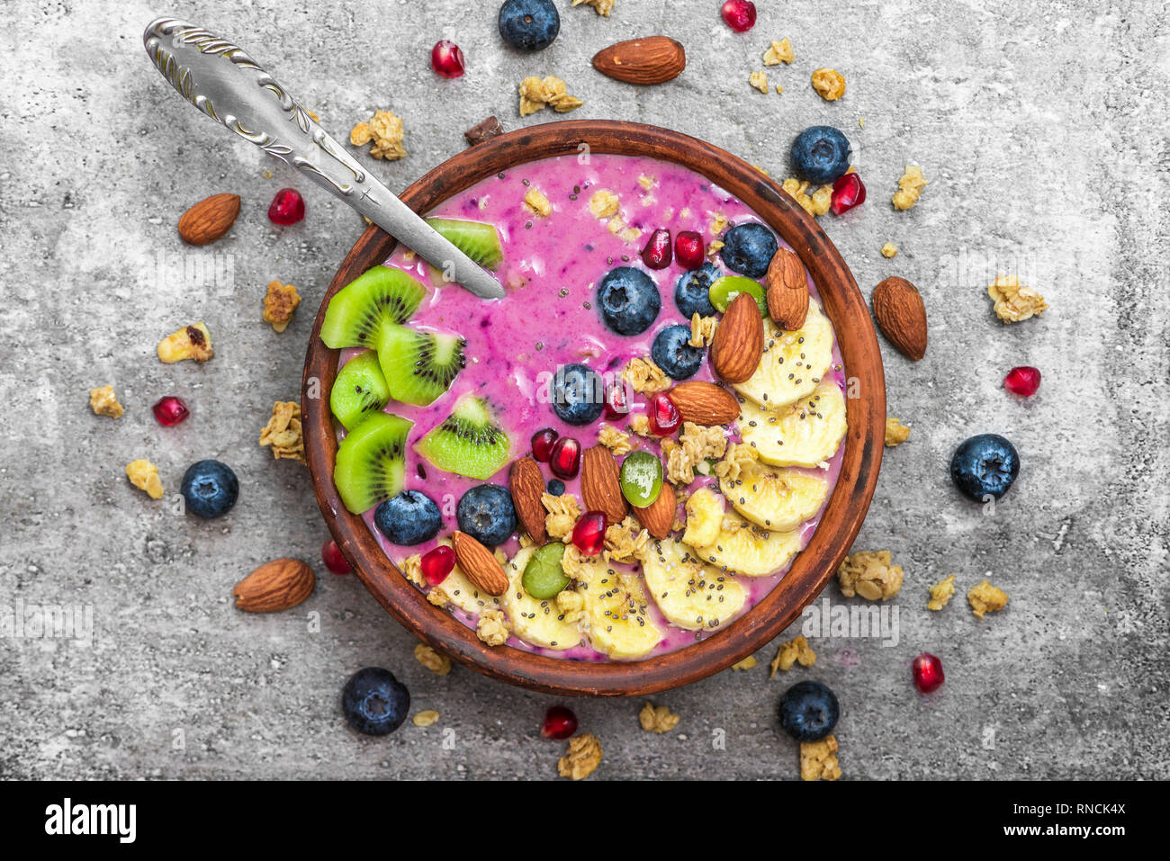 Acai smoothie bowl topped with blueberry, fruits, chia and pumpkin seed, almonds and granola with spoon. healthy vegan breakfast. top view Stock Photo