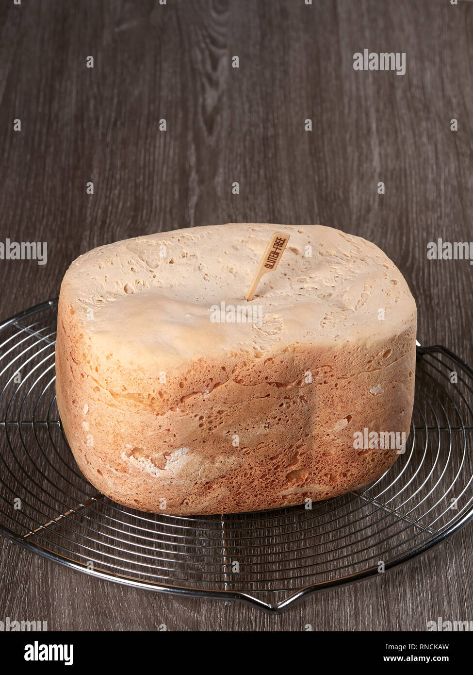 Freshly baked gluten-free bread, made at home with the bread machine, set on a cooling rack, on brown background Stock Photo