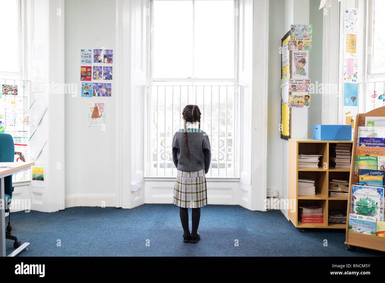 Primary school aged girl standing alone in front of classroom window Stock Photo