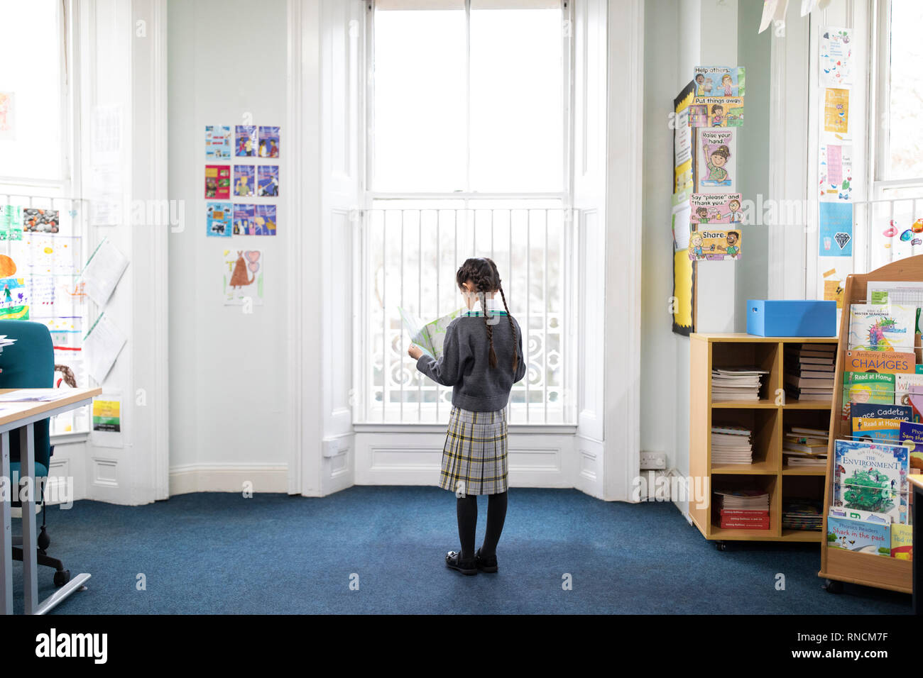 Primary school aged girl reading a book in front of classroom window Stock Photo