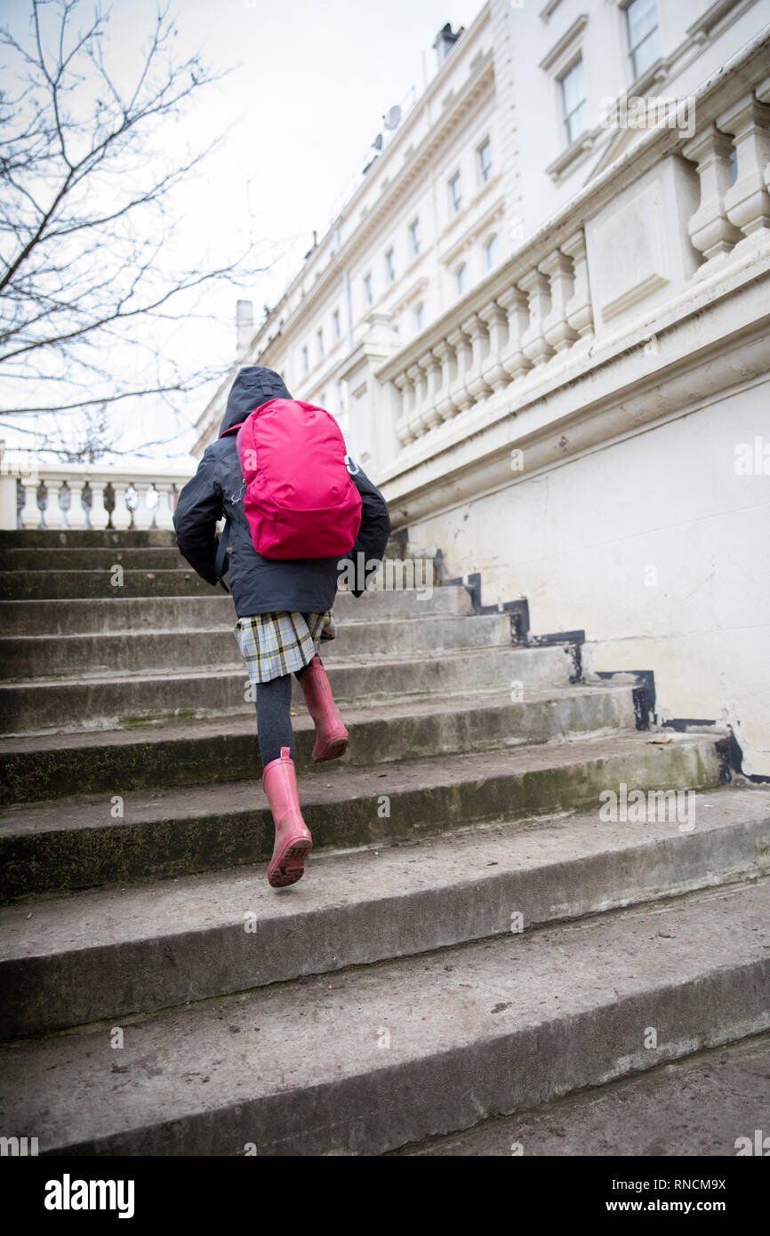 Primary school age girl running up steps to school in affluent urban area Stock Photo