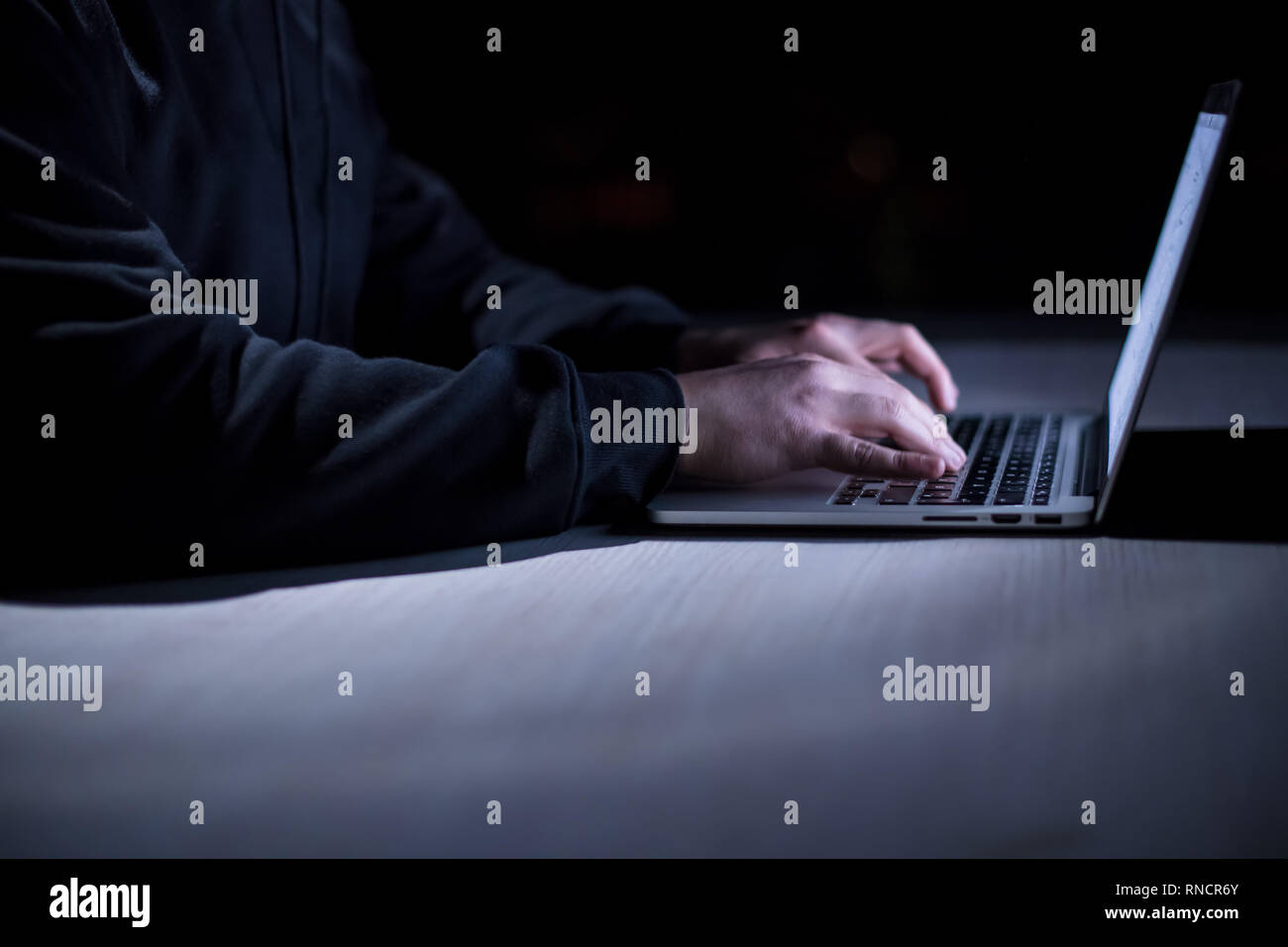 Young talented hacker using laptop computer while working in dark ...